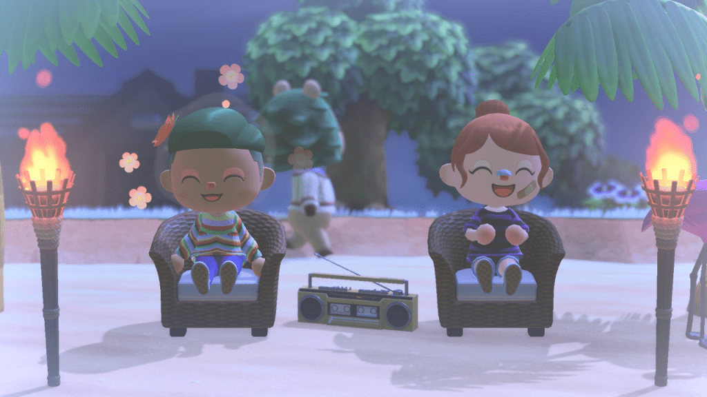 Animal Crossing New Horizons. Two villagers sit at the beach between tiki torches, listening to a boombox and smiling.